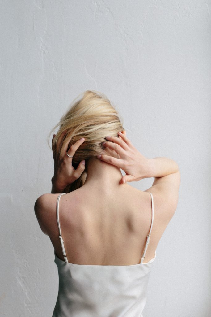 blond woman facing away caresses neck