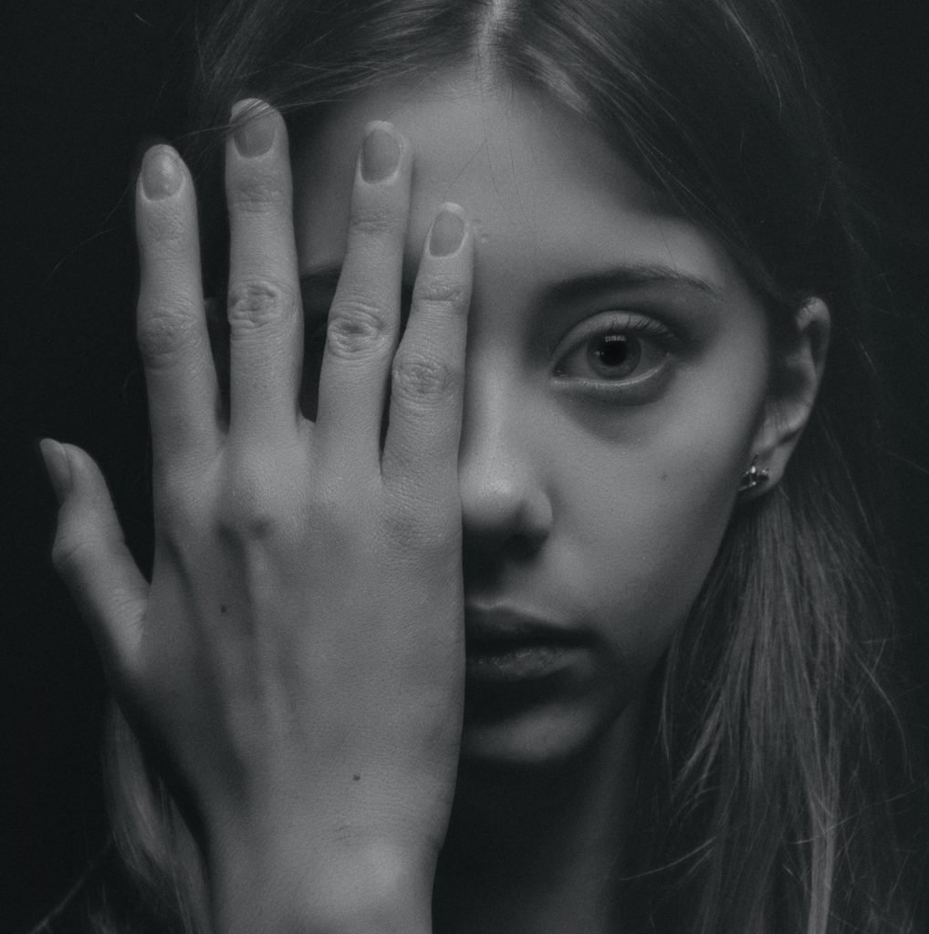 Teen girl looks directly at camera and holds hand over half of her face; black and white image