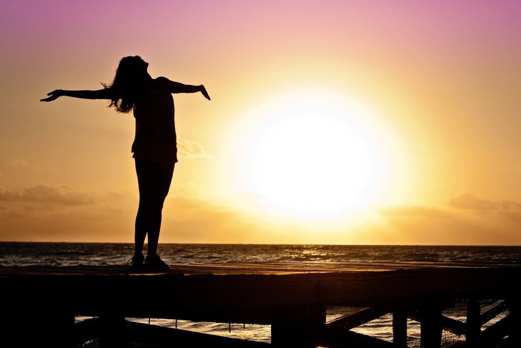 Woman spreads arms with joy on a beach during sunset