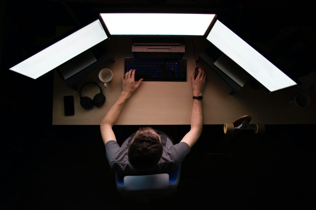 Person viewed from above sits in front of three computer monitors with their hands on the keyboard.