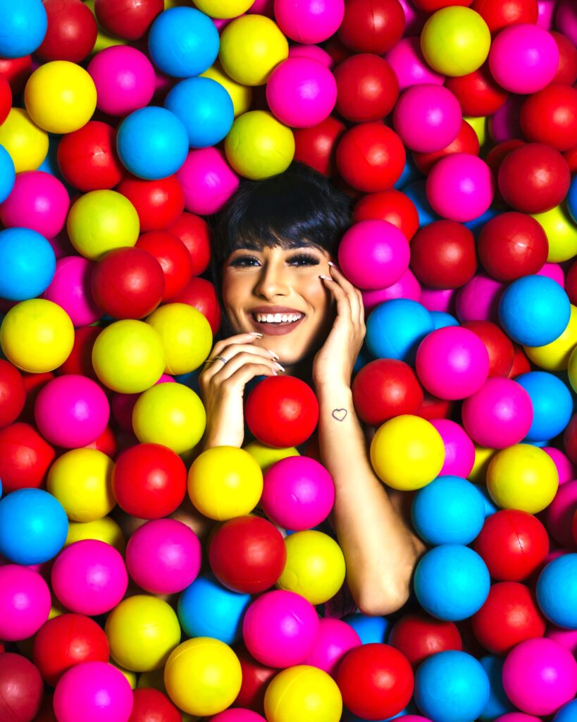 Woman's smiling face and arms emerge from colorful balls in a ball pit