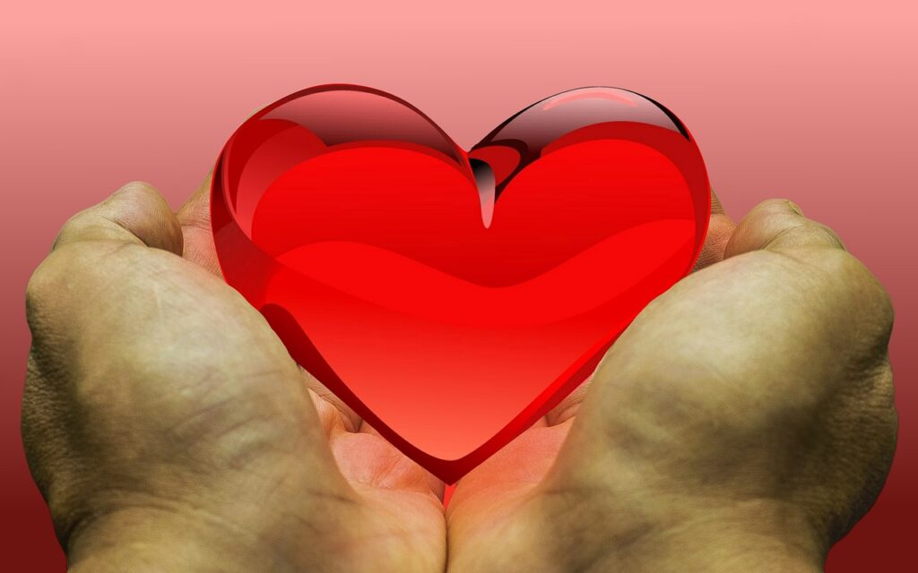two hands hold a clear read heart-shaped object as if to offer or give it to someone.