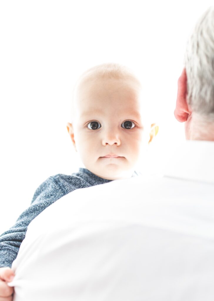 Baby in blue looks into camera over the shoulder of a gray-haired man in a white shirt