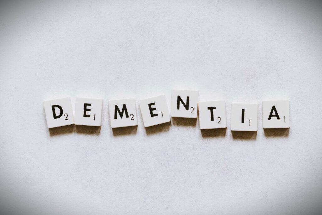 The word Dementia is spelled out using white scrabble tiles on a white background