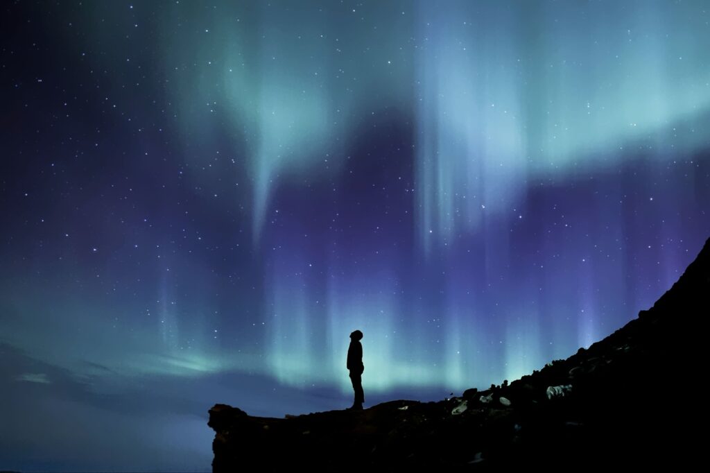 person stands in silhouette gazing up with a backdrop of the northern lights