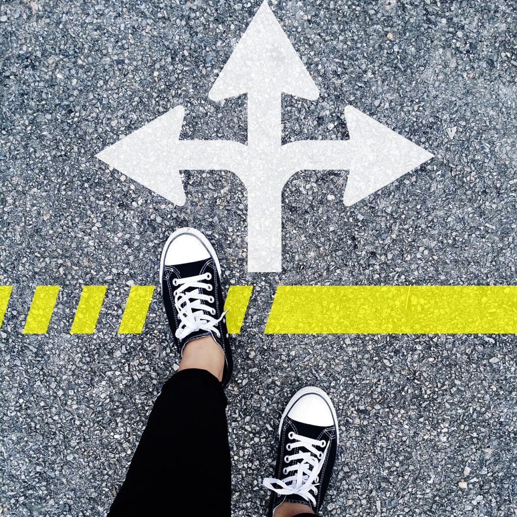 First person point of view of the person's feet standing with arrows painted on concrete pointing in three different directions.