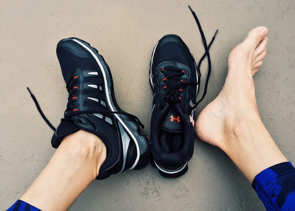 First person perspective looking down at feet with running shoes with no socks and one shoe off.